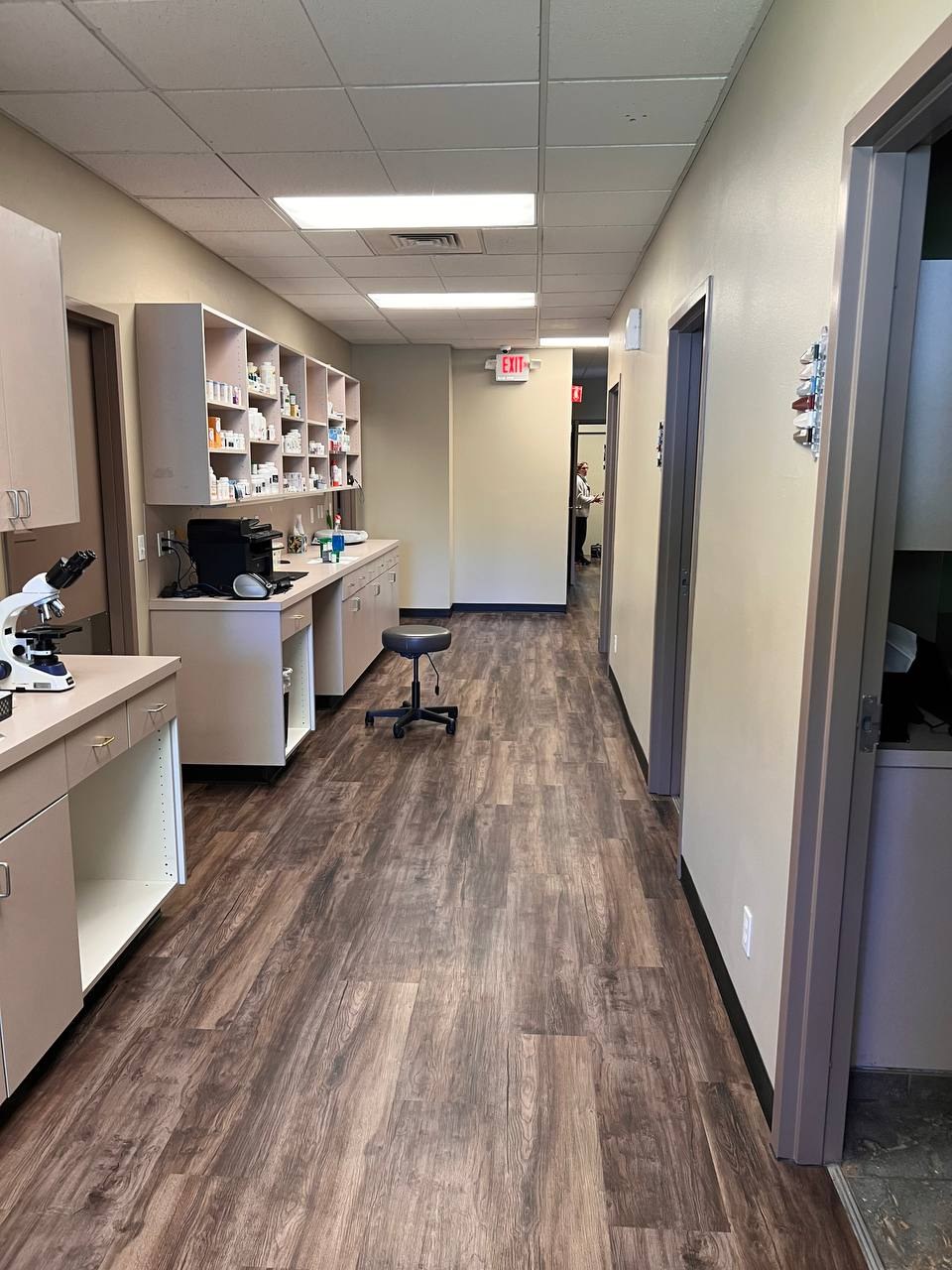 The lab bench with a microscope, pharmacy shelving, and the corridor beyond
